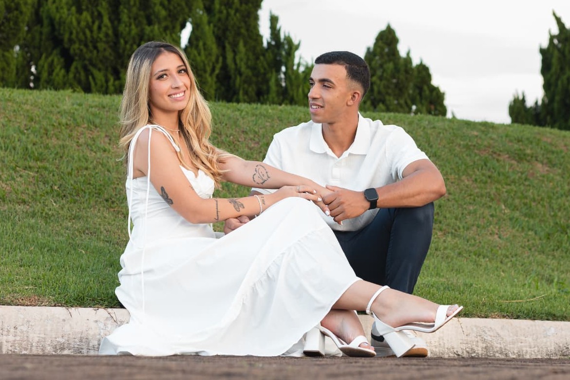 Alysson e Eduarda sentados no gramado, um olhando para o outro